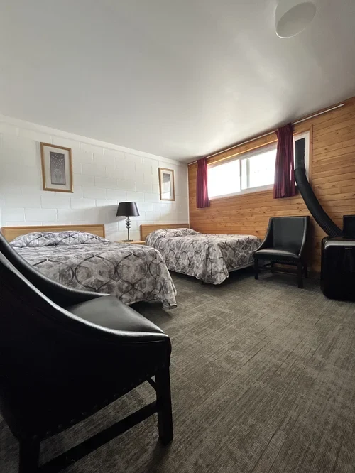 Room with two double beds, wood-panel accent wall and seating